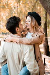 Obraz premium man in trench coat holding in arms stylish woman in hat in autumnal park