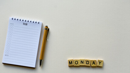 Notepad with pen and wooden word "Monday" on a beige paper background. Top view. Close-up. Flat lay.