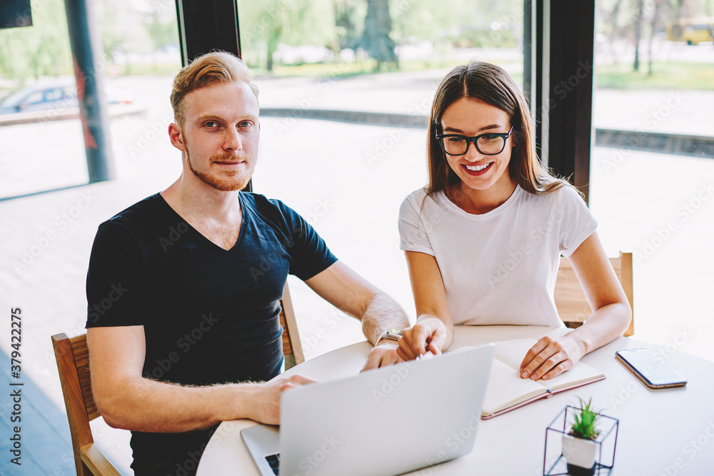 Poster portrait of red hair male programmer looking at camera while happy female colleague in optical spect