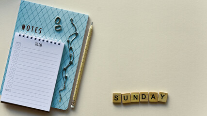Two notepads with pencil, silver bracelet and earrings, wooden word "Sunday" on a beige paper background. Top view. Close-up. Flat lay.