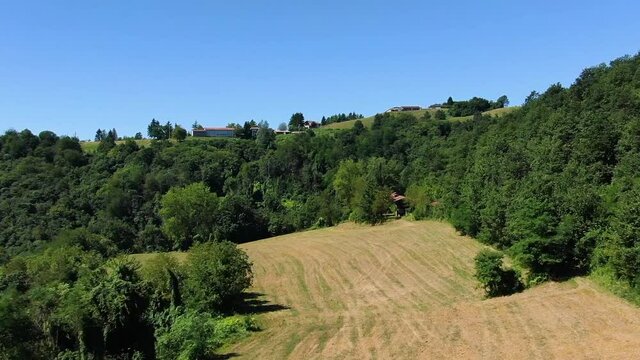 Flying over a plowed field surrounding by wood in a hill in Langhe shire