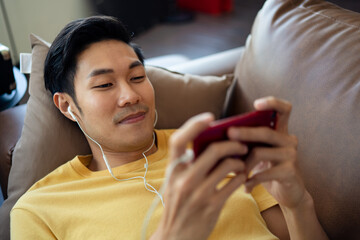 Asian young man in casual style clothes stay at home and relaxing with smartphone on the sofa.