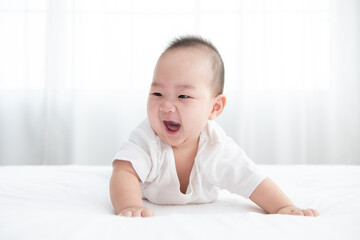 Portrait of a crawling baby on the bed. Happy asian infant in bedroom.