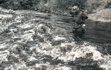 A world war II soldier crosses a stormy river with a rifle on his shoulders.