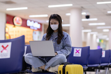 Asian young woman wearing face maks using laptop computer at airport Due Covid-19 flu virus pandemic and protection