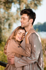 woman with closed eyes hugging man in trench coat outside