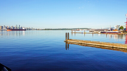 Jetty reflected on tranquil waters at Lonsdale Quay, BC, with Vancouver waterfront and Stanley Park on horizon