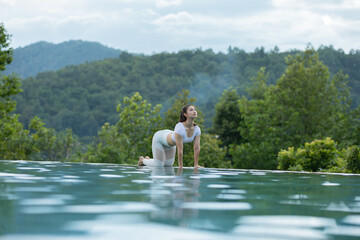 Calm of Athlete Attractive Asian woman relaxing in yoga Cat Cow Pose on the pool above the Mountain peak in front of beautiful nature views,comfortable and relax in vacations