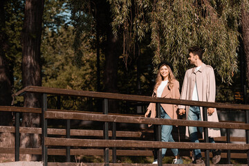 couple in trench coats holding hands and walking on wooden bridge