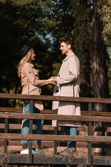 profile of stylish couple in trench coats holding hands on wooden bridge