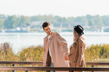 man in trench coat holding hands with woman in hat