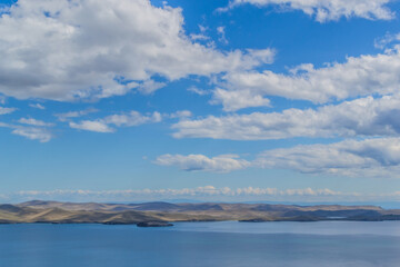 view of the clear calm undulating blue water of Lake Baikal, mountains on the horizon, blue cky, whire clouds