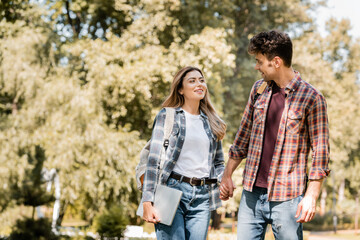 woman in plaid shirt with laptop holding hands with man in park