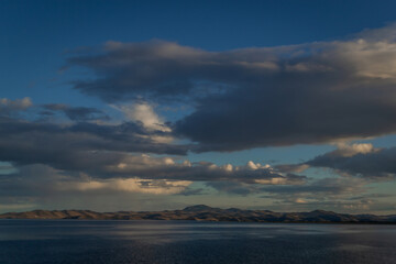 Fototapeta premium view of the clear calm undulating blue water of Lake Baikal, mountains on the horizon, evening, sunset clouds
