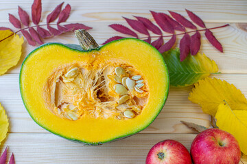Cut ripe, yellow pumpkin on a wooden background with autumn leaves