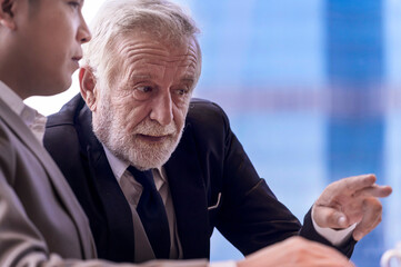 Elder businessman having discuss business plan with young staff at skyscraper office with cityscape business zone background