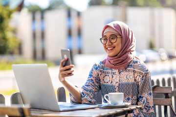 Young Muslim woman using a laptop in outdoor cafe
