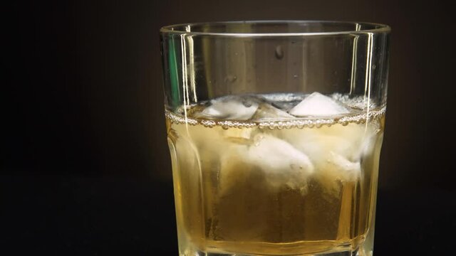 Whiskey falls into a glass with very cold ice 4k close-up