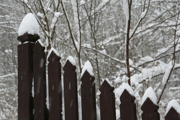 Ciemny drewniany płot z czapami śniegu na sztachetach pośród padającego śniegu na tle...