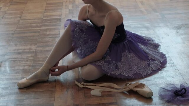 Ballerina is tying ribbons on pointe shoes. Legs of a ballerina close-up.