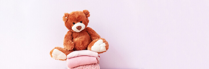 Brown stuffed teddy bear sitting on stack of clean cotton towels or clothes. Childhood care, clothing and plush toy for children in orphanage. Doll for nursery or charity. Website banner, web page