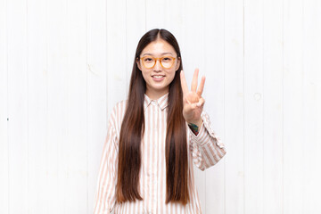 asian young woman smiling and looking friendly, showing number three or third with hand forward,...
