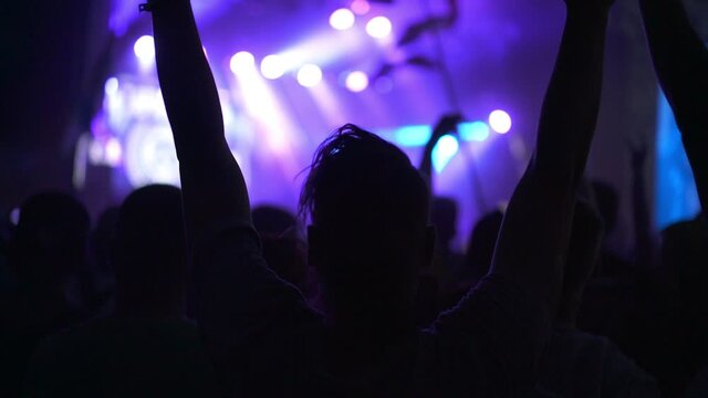 People clapping their hands and singing songs. Silhouette of a girl dancing at a rock band concert. Live performance in a nightclub with fans and stars. Concept of entertainment and background.