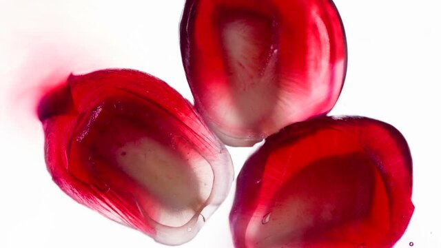 Crushing Three Pomegranate Seeds. Pomegranate seeds are compressed and crushed close-up on a bright white background, creating a juicy splash of pulp and juice. Shooting at 120 fps