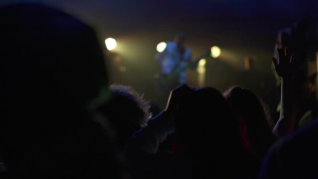 Live concert performance in a club filled with people raising their hands in the air. The concept of partying and fun. Hip-hop star performing on stage in front of fans. Music night gig.