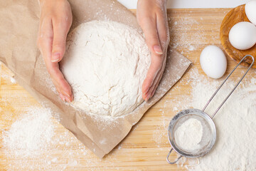 Home cooking concept. Female hands prepare homemade dough on a floured wooden board. Close-up.