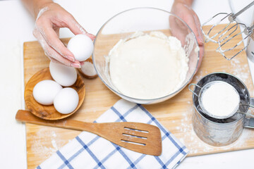 making dough for bread or homemade baked goods. ingredients on the desk. female hands holding an egg