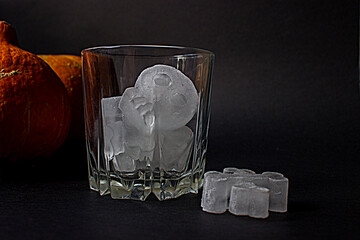 Empty glass with ice, skull and bones for a Halloween party on a dark background with orange...
