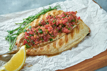Grilled sea bass fish with tomato salsa on a wooden board on a gray background. Cooked seafood