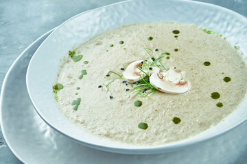 Diet mushroom cream soup with croutons with cheese in a white plate on a gray background