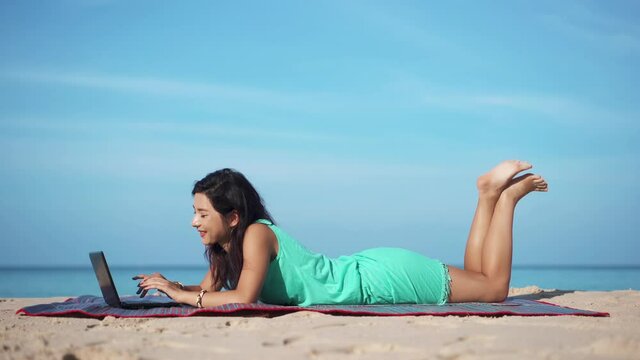 Portrait of pretty woman on beach in front of laptop. Girl freelancer working on computer surrounded by beautiful tropical landscape. Concept of travel.