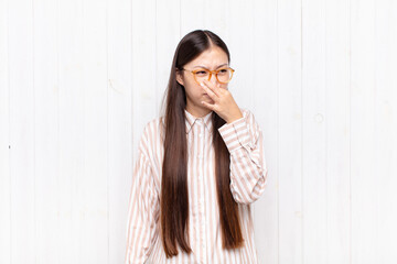 asian young woman feeling disgusted, holding nose to avoid smelling a foul and unpleasant stench