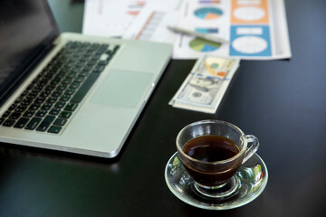 Business computer office desk with desktop laptop, money, and annual, summary report, coffee place on black table, working space at home. Business executive office table concept.