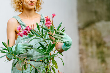 Positive charming female gardener wear mint gloves caressing blooming oleander tree in pot at backyard, outdoor. Change of activity the best rest. - obrazy, fototapety, plakaty