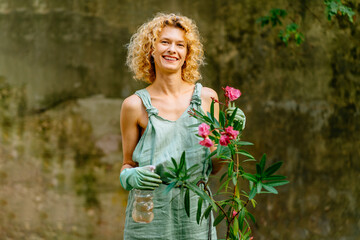 Portrait of positive charming female gardener wear mint gloves caressing blooming oleander tree in...