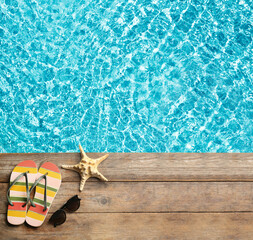 Beach accessories on wooden deck near swimming pool, flat lay. Space for text