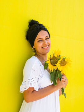 Vertical shot of an attractive Brazilian female with sunflowers on yellow background