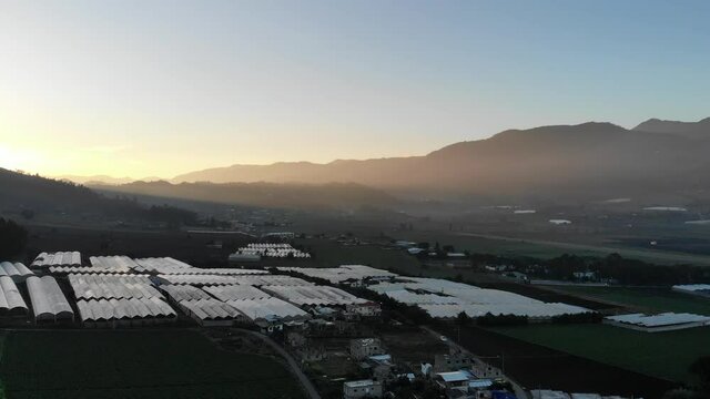 Sideways aerial drone panoramic fly over valley in mountains with greenhouses at sunset in Constanza, Dominican Republic 