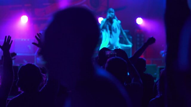 Hip-hop star performing on stage in front of fans. Live concert performance in a club filled with people raising their hands in the air. The concept of partying and fun. Music night gig.
