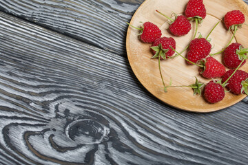 Raspberries with tails lie on a wooden saucer. On black boards, with an expressive woody texture.