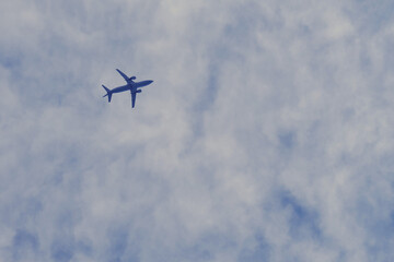 Airplane in the blue sky with clouds, bottom view