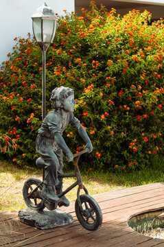 The outside lapm with the statue of a boy riding a bicycle as a exterior detail of a garden over the background of bush with orange flowers
