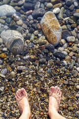 feet on the beach on the shore of the beach with rocks pebbles. vertical photo