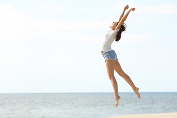 Fototapeta na wymiar Excited woman with long legs jumping on the beach