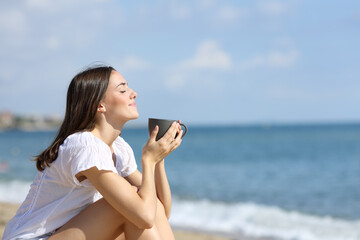 Girl smelling coffee on the beach on summer