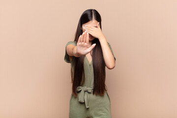 asian young woman covering face with hand and putting other hand up front to stop camera, refusing...